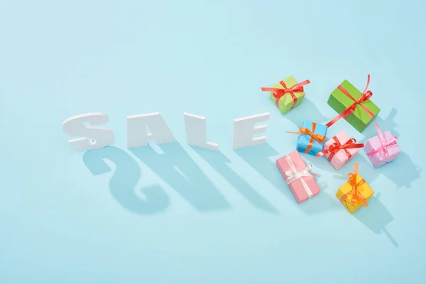 Vista superior de letras de venta blanca con sombras y cajas de regalo festivas sobre fondo azul - foto de stock