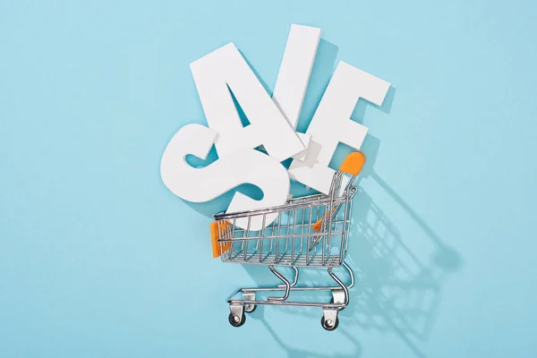Top view of white sale lettering in decorative shopping cart on blue background — Stock Photo