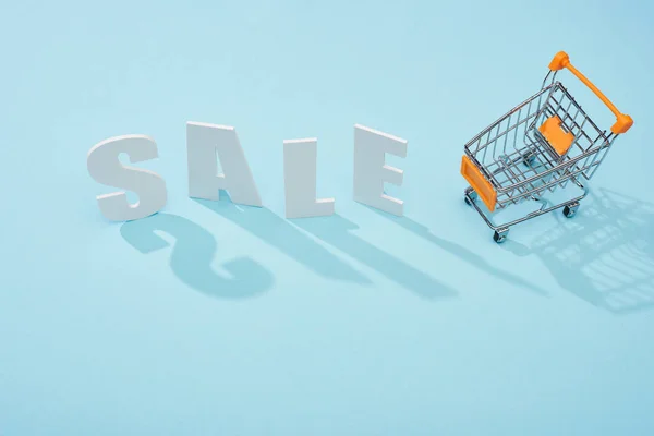 Top view of white sale lettering near shopping trolley on blue background — Stock Photo