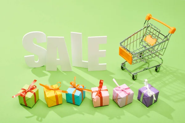 Weißer Verkauf Schriftzug in der Nähe von dekorativen Geschenkboxen und Einkaufswagen auf grünem Hintergrund — Stockfoto