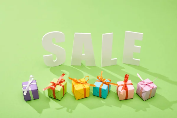 White sale lettering near decorative festive gift boxes on green background — Stock Photo