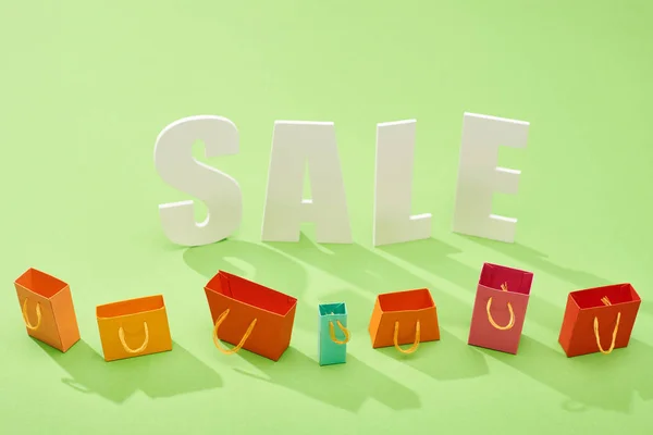 Bolsas de compras coloridas decorativas y letras de venta sobre fondo verde - foto de stock