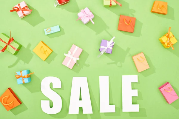 Top view of scattered decorative gift boxes and shopping bags on green background with sale word — Stock Photo