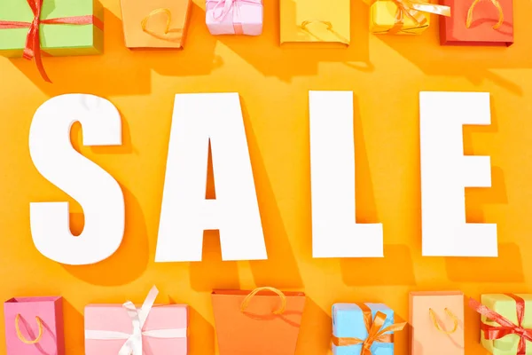 Vista superior de la venta de letras blancas cerca de bolsas de compras y regalos sobre fondo naranja brillante - foto de stock