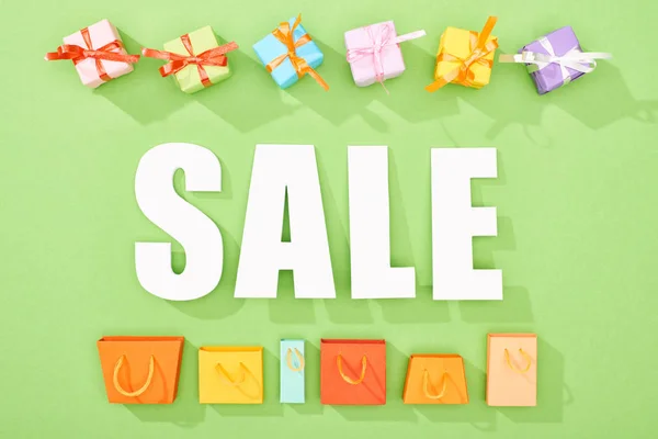 Draufsicht auf dekorative Geschenkboxen und Einkaufstaschen auf grünem Hintergrund mit Verkauf Schriftzug — Stockfoto