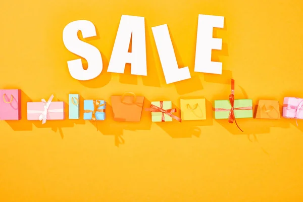 Vista dall'alto di vendita bianca lettering sopra borse della spesa e regali su sfondo arancione brillante con spazio copia — Foto stock