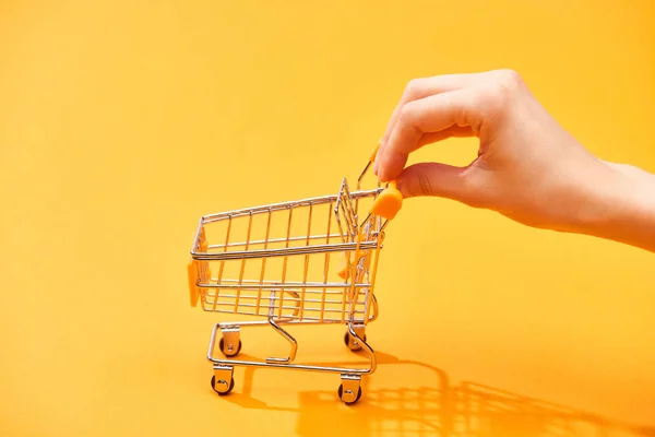 Cropped view of woman pushing small shopping cart on bright orange background — Stock Photo