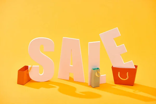 White sale lettering near shopping bags on bright orange background — Stock Photo