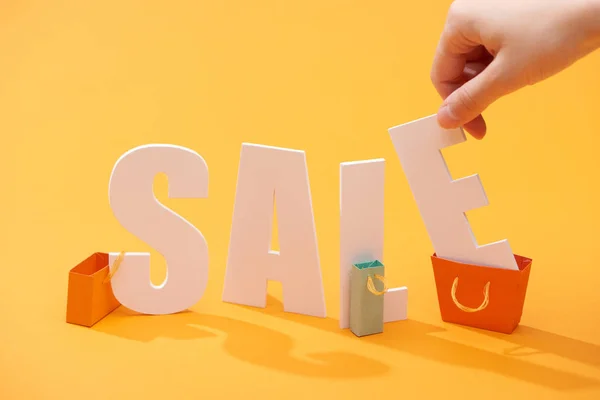 Vista cortada do homem segurando carta de venda branca lettering perto de sacos de compras no fundo laranja — Fotografia de Stock