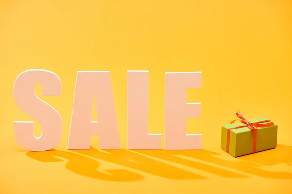 White sale lettering near wrapped gift box on bright orange background — Stock Photo