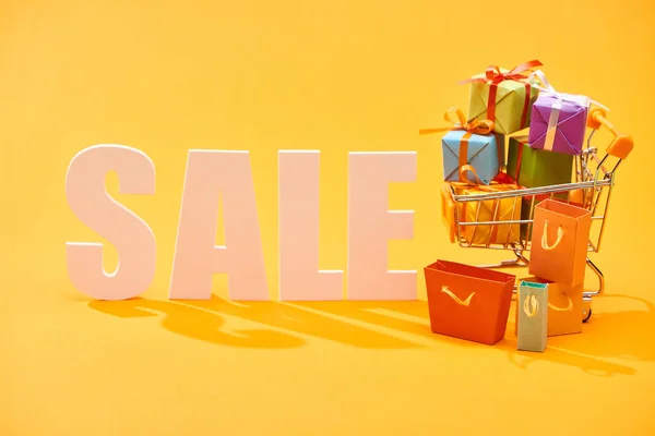 White sale lettering with shopping bags and festive gifts in shopping cart on bright orange background — Stock Photo