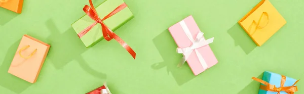 Vue du dessus des boîtes-cadeaux dispersées et des sacs à provisions sur fond vert, vue panoramique — Photo de stock