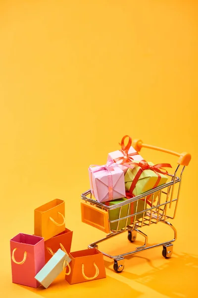 Shopping cart with presents near shopping bags on bright orange background — Stock Photo