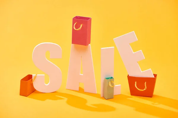 White sale lettering with shopping bags on bright orange background — Stock Photo