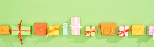 Pose plate avec des boîtes-cadeaux et des sacs à provisions sur fond vert, panoramique — Photo de stock