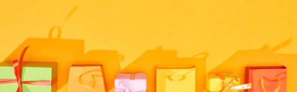 Вид сверху на праздничные завернутые подарки и сумки для покупок на ярко-оранжевом фоне, панорамный снимок — стоковое фото
