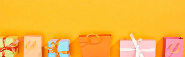 Tiro panorâmico de sacos de compras e presentes embrulhados festivos no fundo laranja brilhante — Fotografia de Stock
