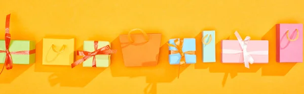 Plan panoramique de sacs à provisions et cadeaux emballés festifs en rangée sur fond orange vif — Photo de stock