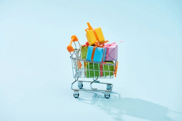 Festive wrapped presents in shopping cart on blue background — Stock Photo