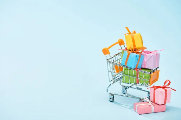 Festive wrapped presents in shopping cart on blue background with copy space — Stock Photo
