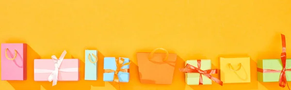 Panoramic shot of shopping bags and wrapped gifts on bright orange background — Stock Photo