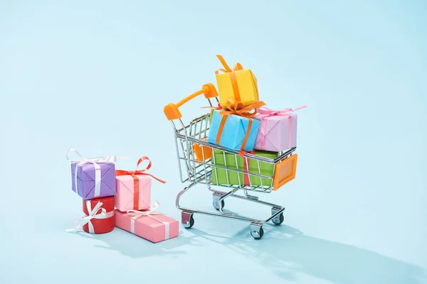 Festive wrapped gifts in shopping cart on blue background — Stock Photo