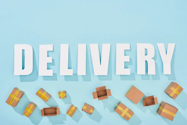 Top view of white word delivery near open and closed cardboard boxes on blue background — Stock Photo