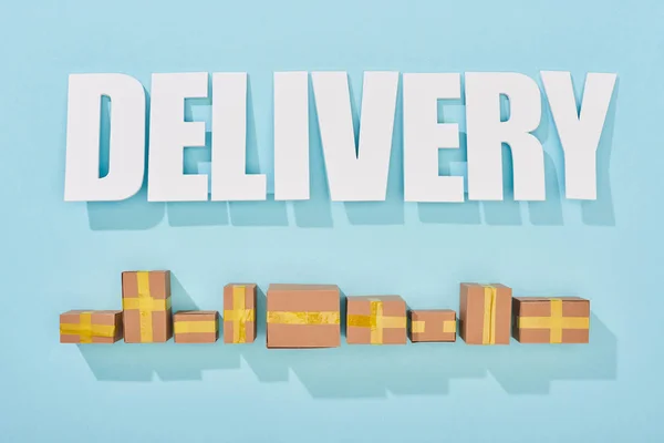 Delivery inscription with shadows near closed cardboard boxes on blue background with copy space — Stock Photo