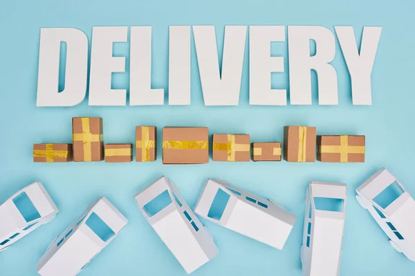 Delivery inscription near closed cardboard boxes and mini vans on blue background — Stock Photo