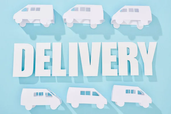 White mini vans around delivery inscription with shadows near blue background — Stock Photo