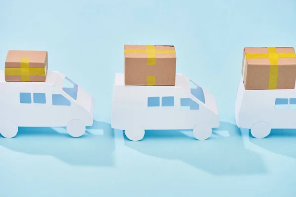 Mini furgonetas blancas con cajas de cartón cerradas sobre fondo azul - foto de stock