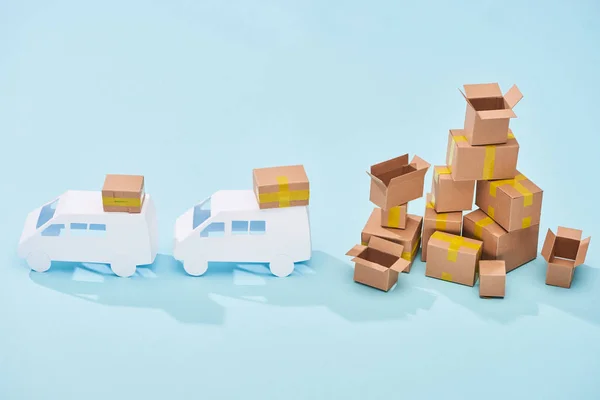 White mini vans near pile of cardboard boxes on blue background — Stock Photo