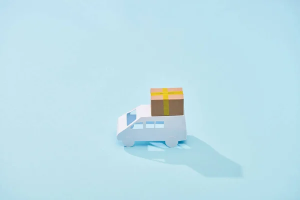 Mini furgoneta blanca con paquete de cartón sobre fondo azul - foto de stock
