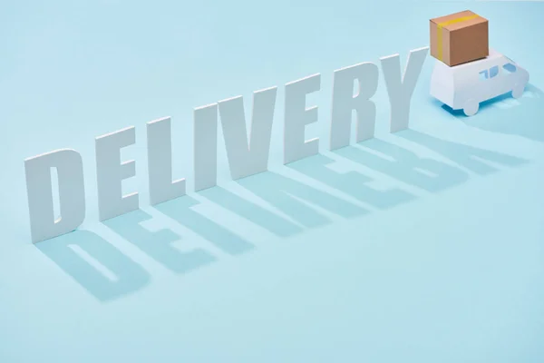 Delivery inscription near white mini truck with cardboard box on blue background — Stock Photo