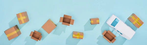 Panoramic shot of closed and open cardboard parcels near mini van on blue background — Stock Photo