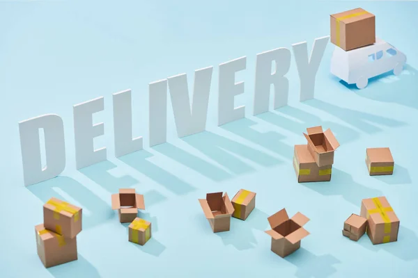 Білий напис доставки поблизу міні вантажівки з картонними коробками на синьому фоні — стокове фото