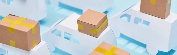 Panoramic shot of cardboard boxes on mini trucks on blue background — Stock Photo