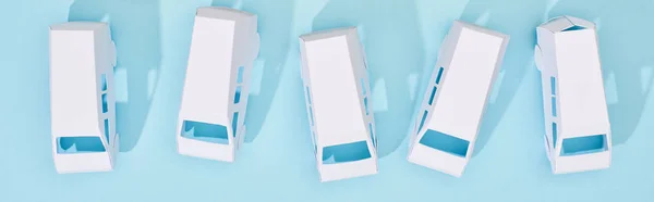 Панорамний знімок мініатюрних білих вантажівок на синьому фоні — стокове фото