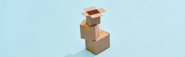 Panoramic shot of cardboard boxes one on top of each other on blue background — Stock Photo