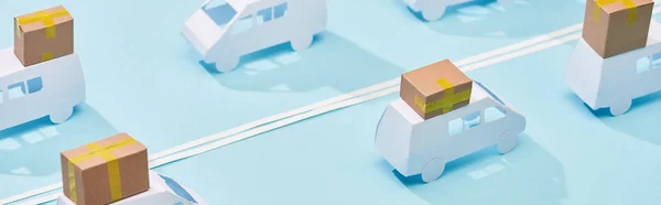 Panoramic shot of miniature trucks with cardboard parcels on blue background with double line — Stock Photo