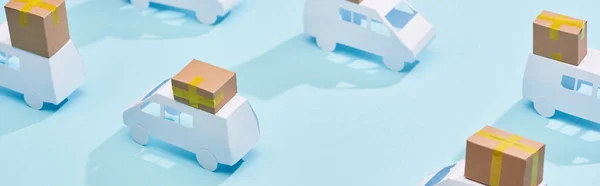 Plano panorámico de camiones en miniatura con cajas de cartón sobre fondo azul - foto de stock