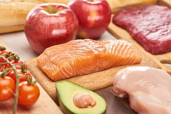 Poisson cru frais, volaille, viande sur planches à découper en bois près des pommes, branche de tomates cerises et la moitié de l'avocat — Photo de stock