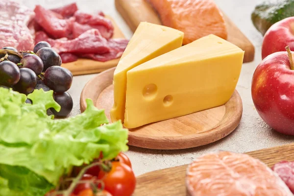Cheese on wooden cutting board near assorted meat, fish fruits and vegetables — Stock Photo