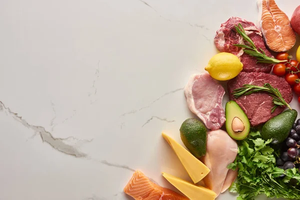 Top view of assorted raw meat, poultry and fish with avocados, lemon, cheese, tomatoes, grapes and greenery twigs — Stock Photo