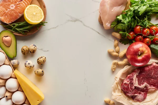 Верхний вид сырого мяса, птицы и рыбы с яйцами, авокадо, лимоном, сыром, веткой помидоров, арахисом и зелеными ветками — стоковое фото