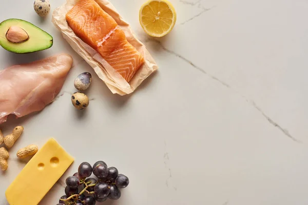 Top view of raw poultry and fish fillet with avocado, lemon, cheese, eggs and grapes — Stock Photo