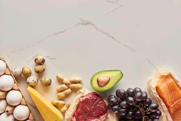 Vista superior de carne cruda y pescado con huevos, aguacate, queso, uvas y cacahuetes - foto de stock