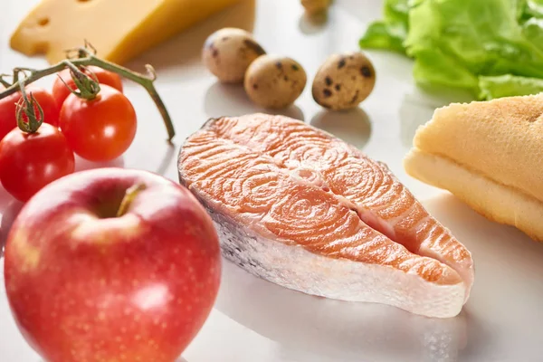 Close up view of raw salmon steak near branch of cherry tomatoes, quail eggs and apple on white surface — Stock Photo