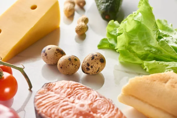 Close up view of raw salmon steak near quail eggs, cheese, lettuce, tomatoes and peanuts on white surface — Stock Photo