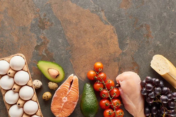 Top view of raw fish and poultry near vegetables, fruits, eggs, baguette and olive oil on marble surface with copy space — Stock Photo